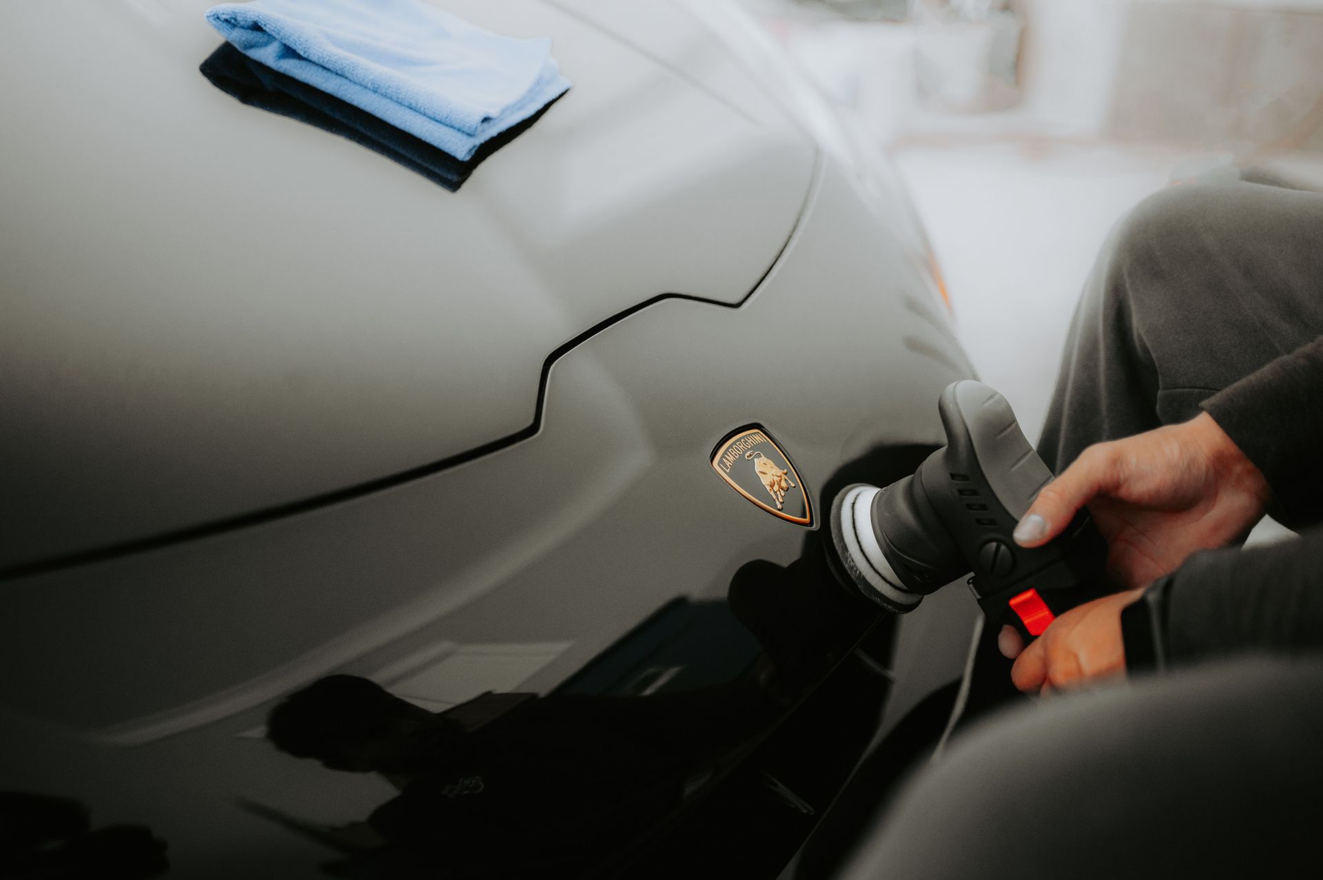 Hand polishing a gray car with a buffer, cleaning cloth on the hood