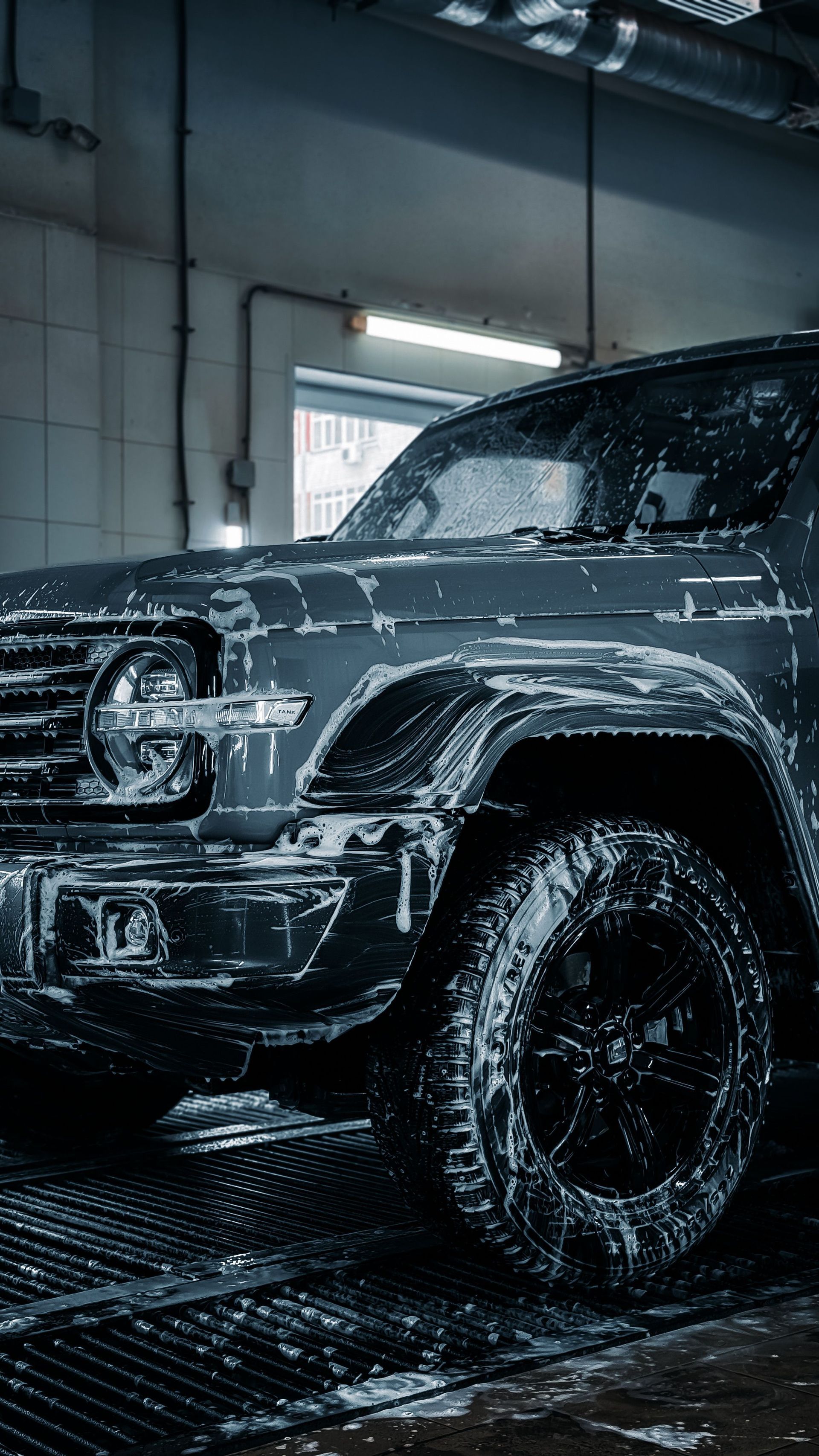 Black off-road SUV being washed in an indoor car wash, covered in soap suds.