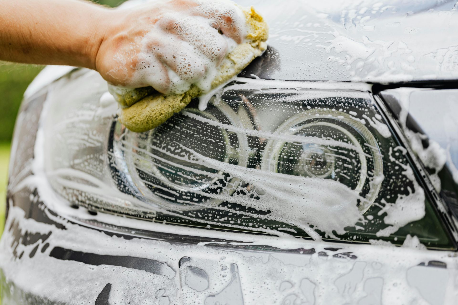 Man polishing a dark blue car with a buffer in a bright auto shop