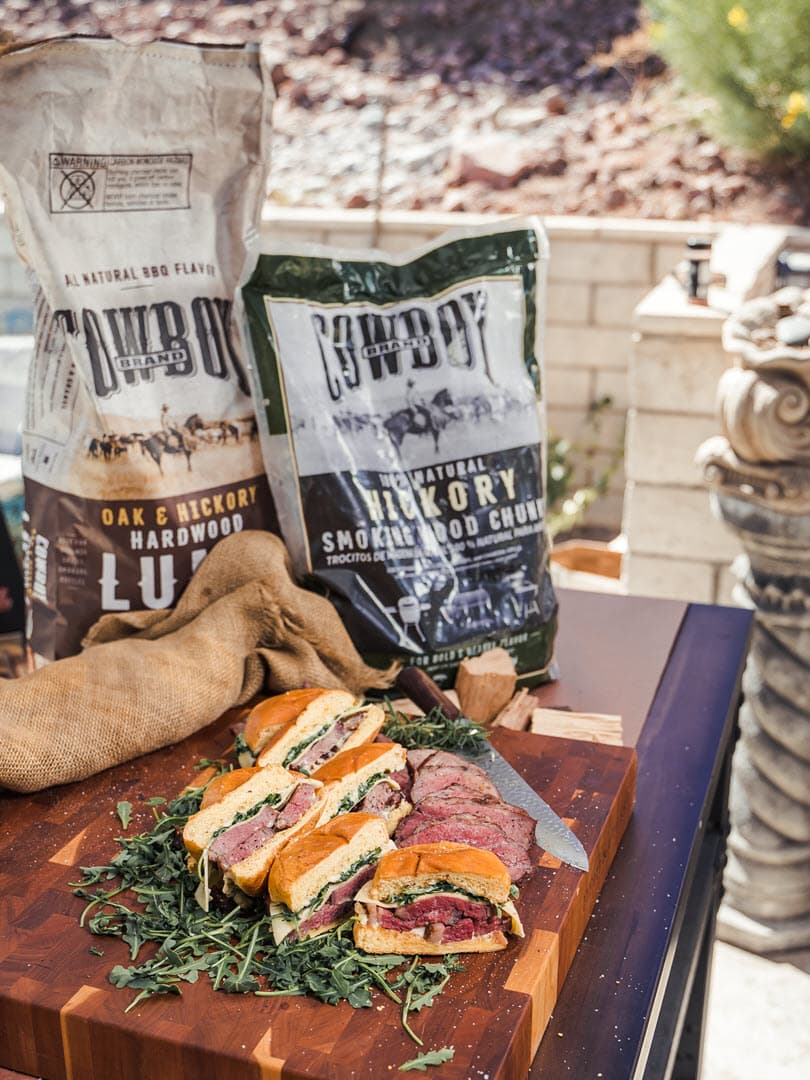 Tri-tip sandwiches  cut on a cutting board with bags of Cowboy Lump and Hickory chunks in background