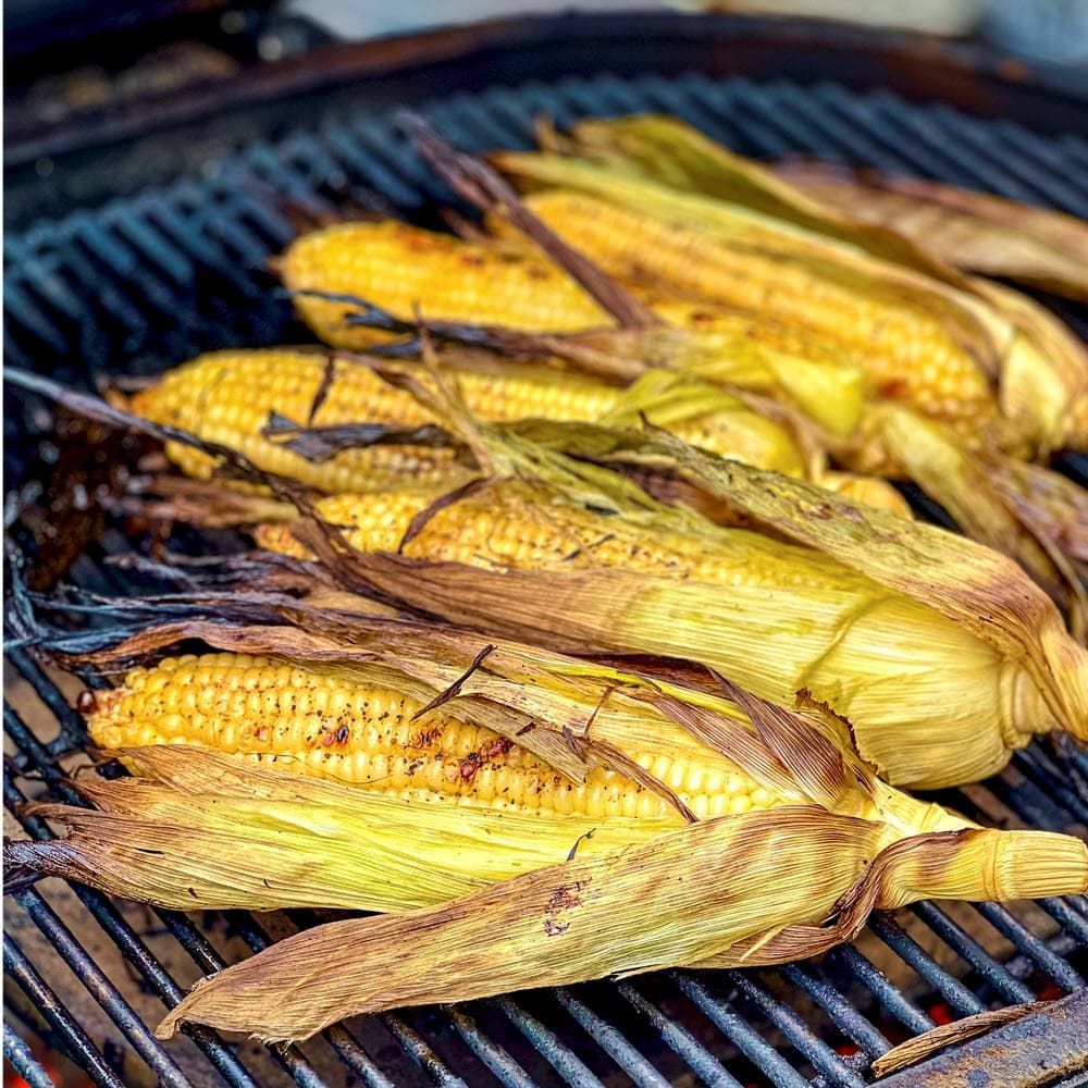 Grilled corn on the cob in husks on a barbecue grate