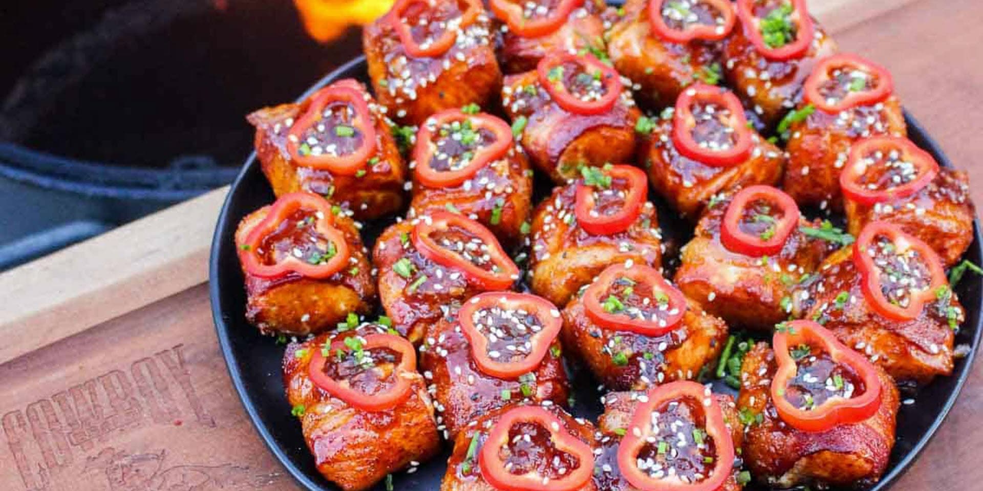 Bacon-wrapped salmon bites garnished with peppers and sesame seeds 
