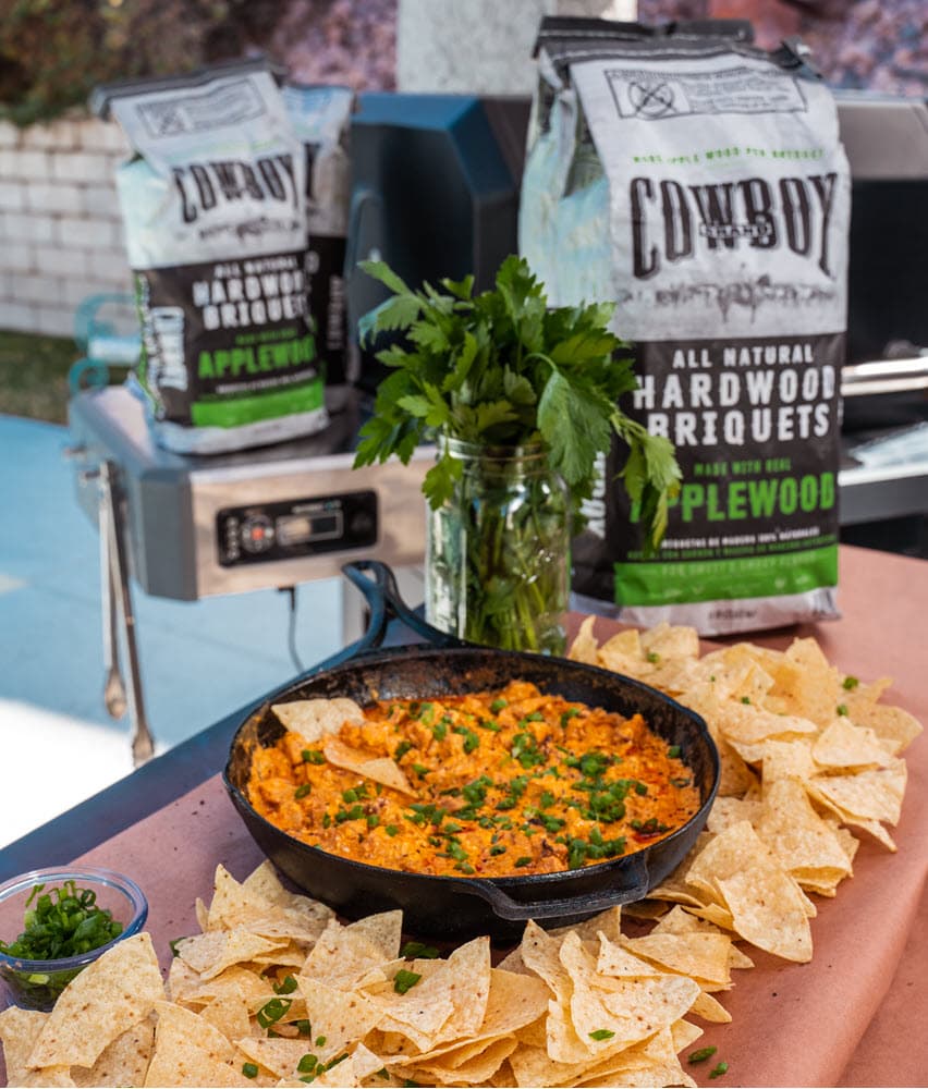 Smoked Buffalo Chicken Dip with tortilla chips, and a bag of Applewood Hardwood briquets in background