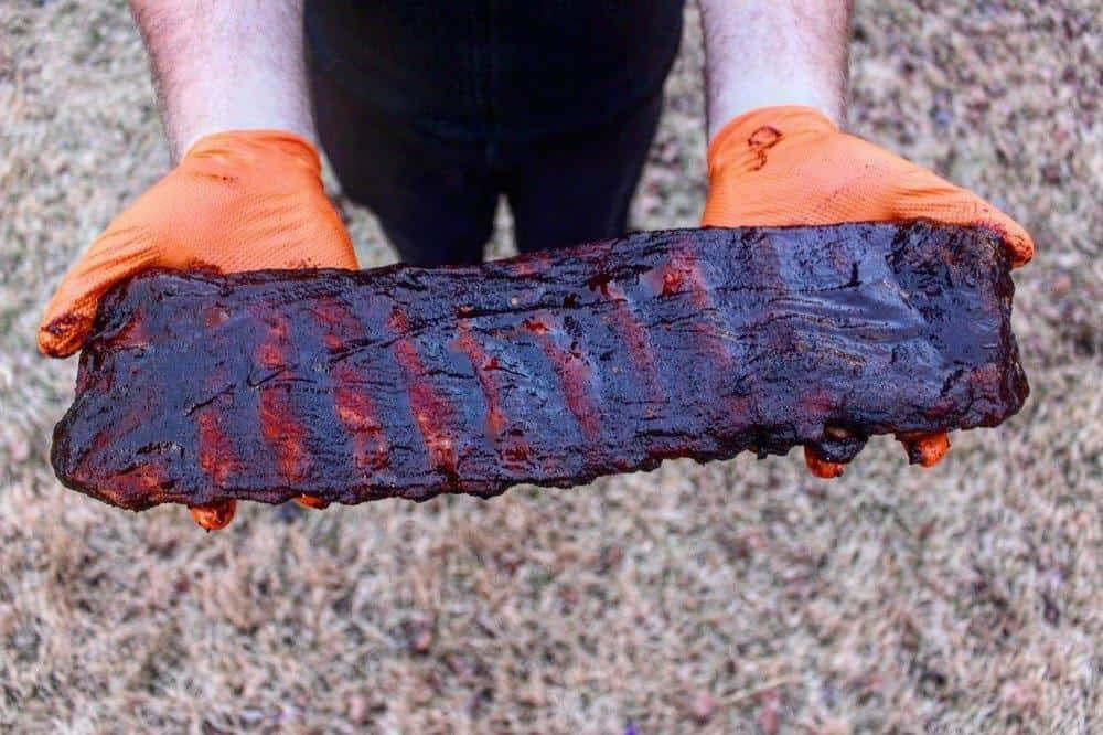hands holding out a whole rack of spicy bbq ribs