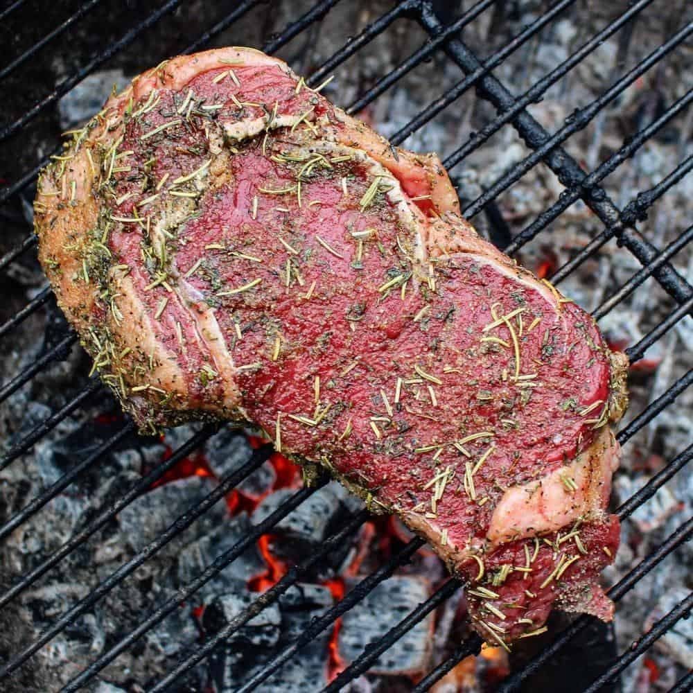 raw Bison ribeye steak cooking on the grill over live fire