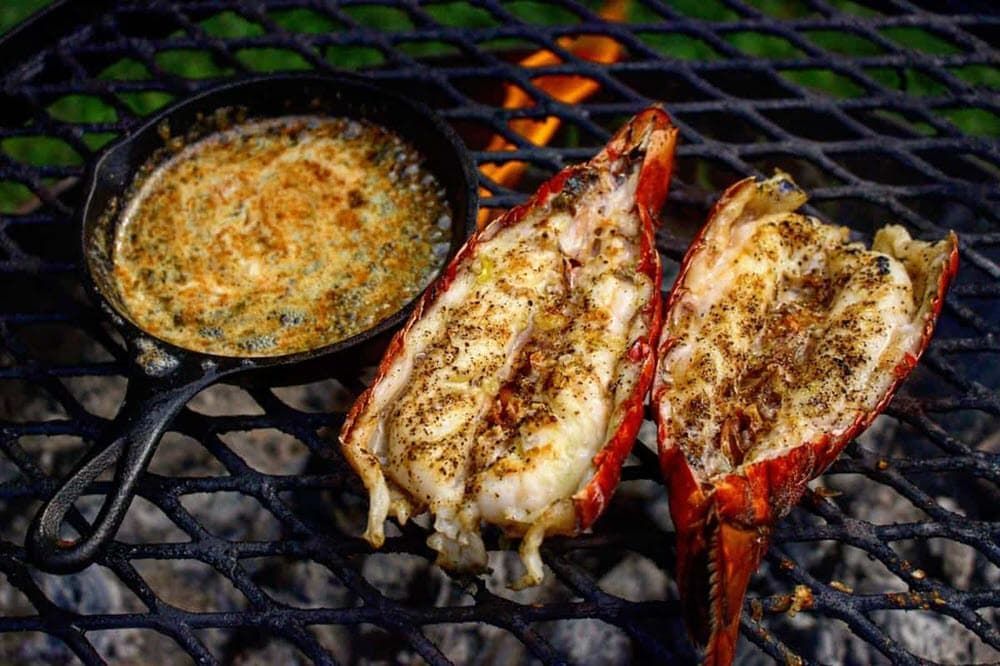 lobster tails in their shells and chive butter sauce in a cast iron grill cooking on the grill