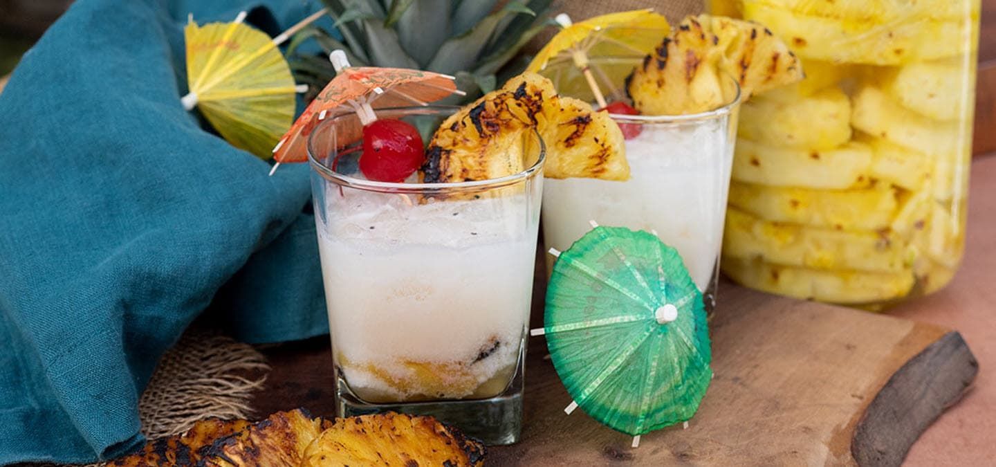 Grilled pina colada cocktails with a grilled pineapple slice and cherry garnish