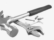 Picture of a wrench, hammer and a screw bits an nails in a pile on the ground.