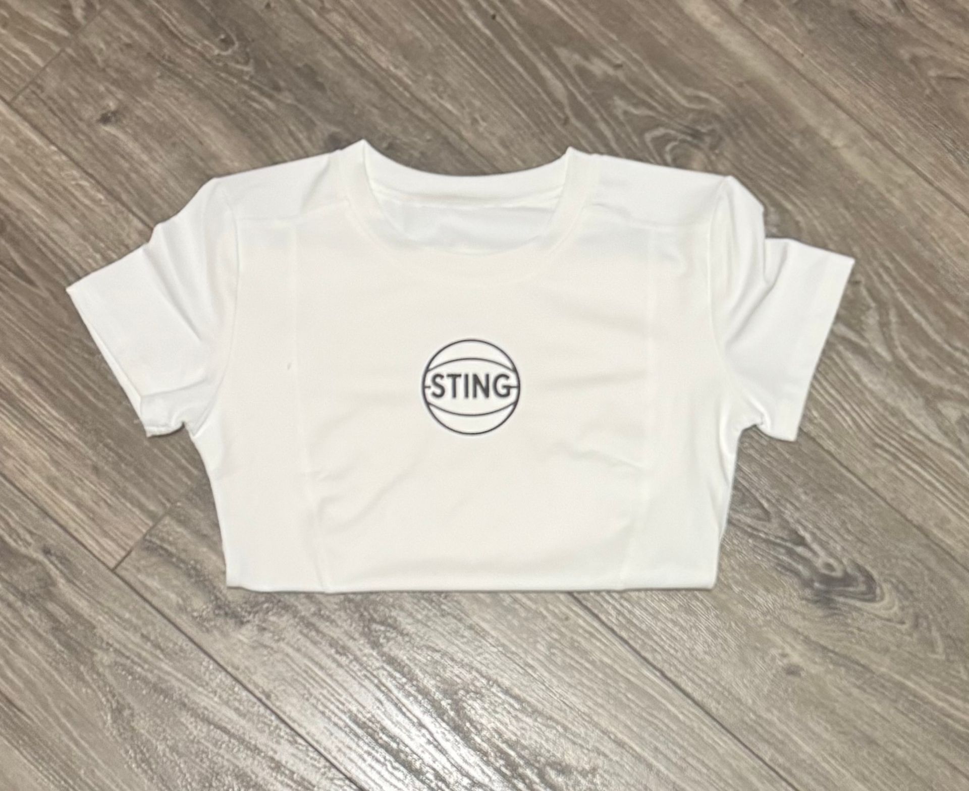 White cropped T-shirt with STING logo laid flat on a wood floor.