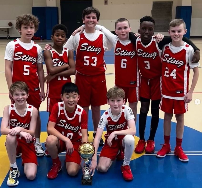 Youth basketball team in red uniforms posing with a trophy on an indoor court.