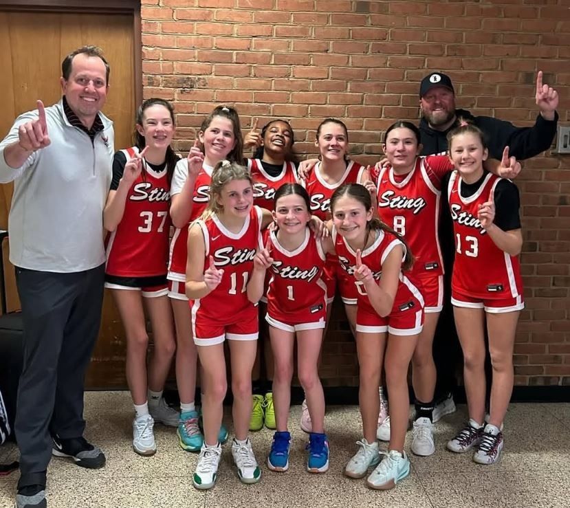 Youth basketball team and coaches posing indoors in red uniforms, smiling in front of a brick wall.