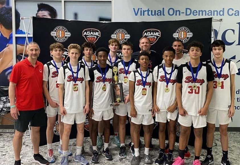 Youth basketball team posing with medals and trophy banners at an event booth.