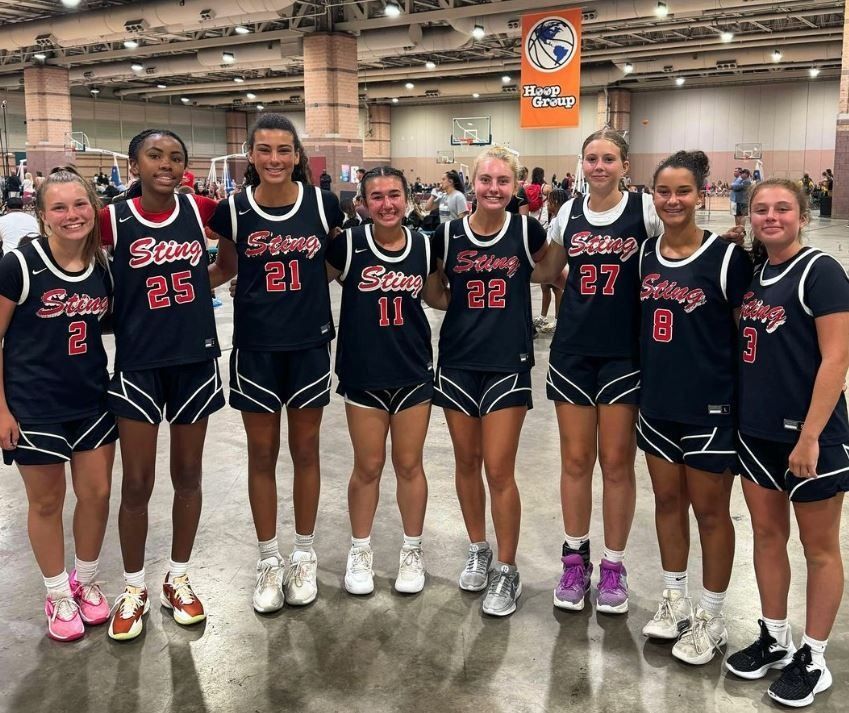 Nine basketball players in black jerseys posing together indoors at a sports event.