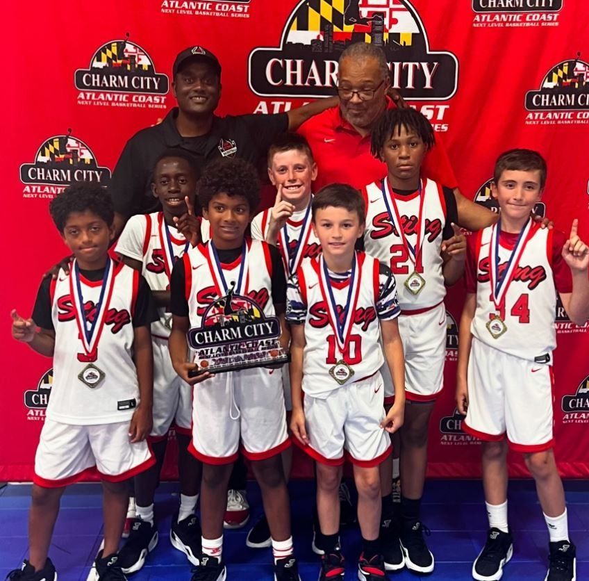 Youth basketball team posing with coaches in front of a Charm City Athletic Club backdrop, wearing medals and uniforms
