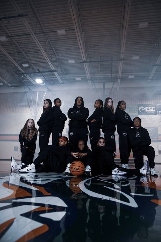 Basketball team posing on a gym court under arena lights, with a basketball in front.