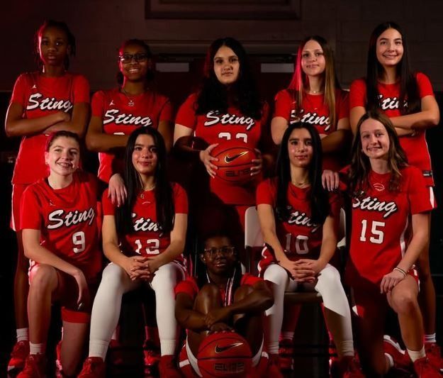 Women's basketball team in red uniforms posing in a studio with a ball, smiling for a team photo.