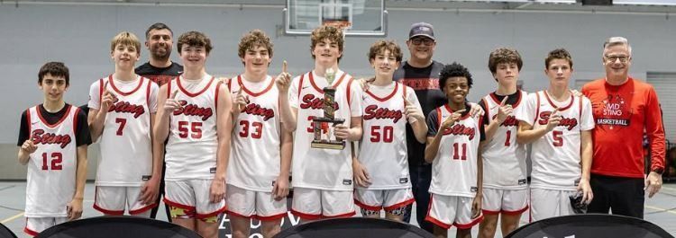 Group of basketball players in white and red uniforms posing with a coach indoors