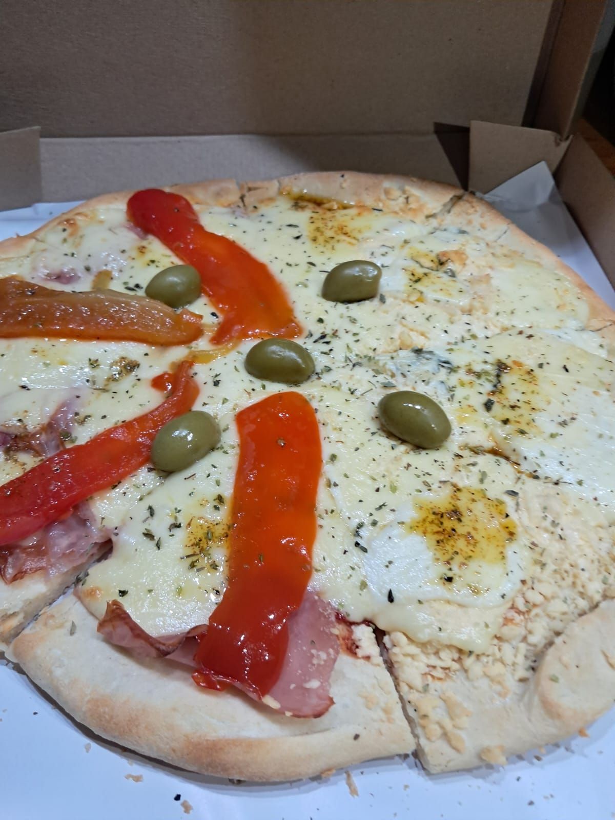 Pizza parcialmente consumida en una caja, cubierta con pimientos, aceitunas y hierbas.