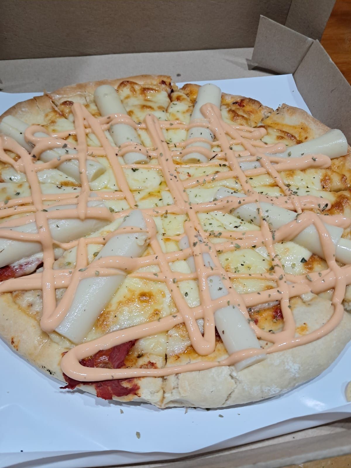 Pizza servida en una caja de cartón con un chorrito de salsa de naranja y trocitos de ingredientes.
