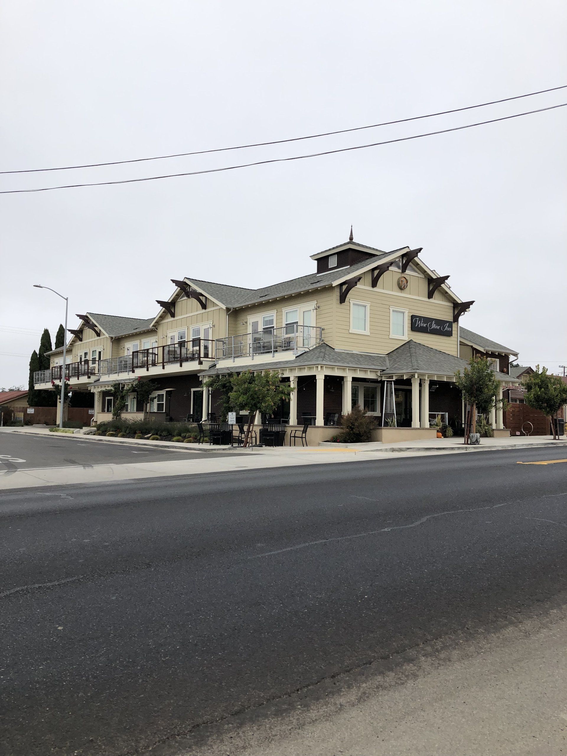 Corner street view of a beige, two-story historic building with shops and awnings under a cloudy sky.