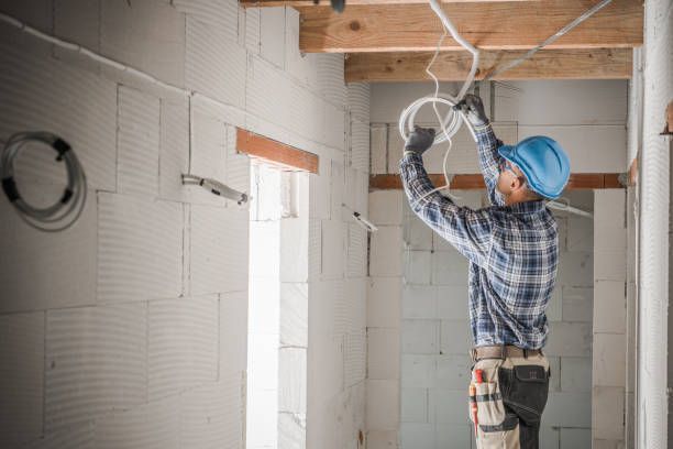 Worker in a blue hard hat installing wiring in an unfinished room under construction