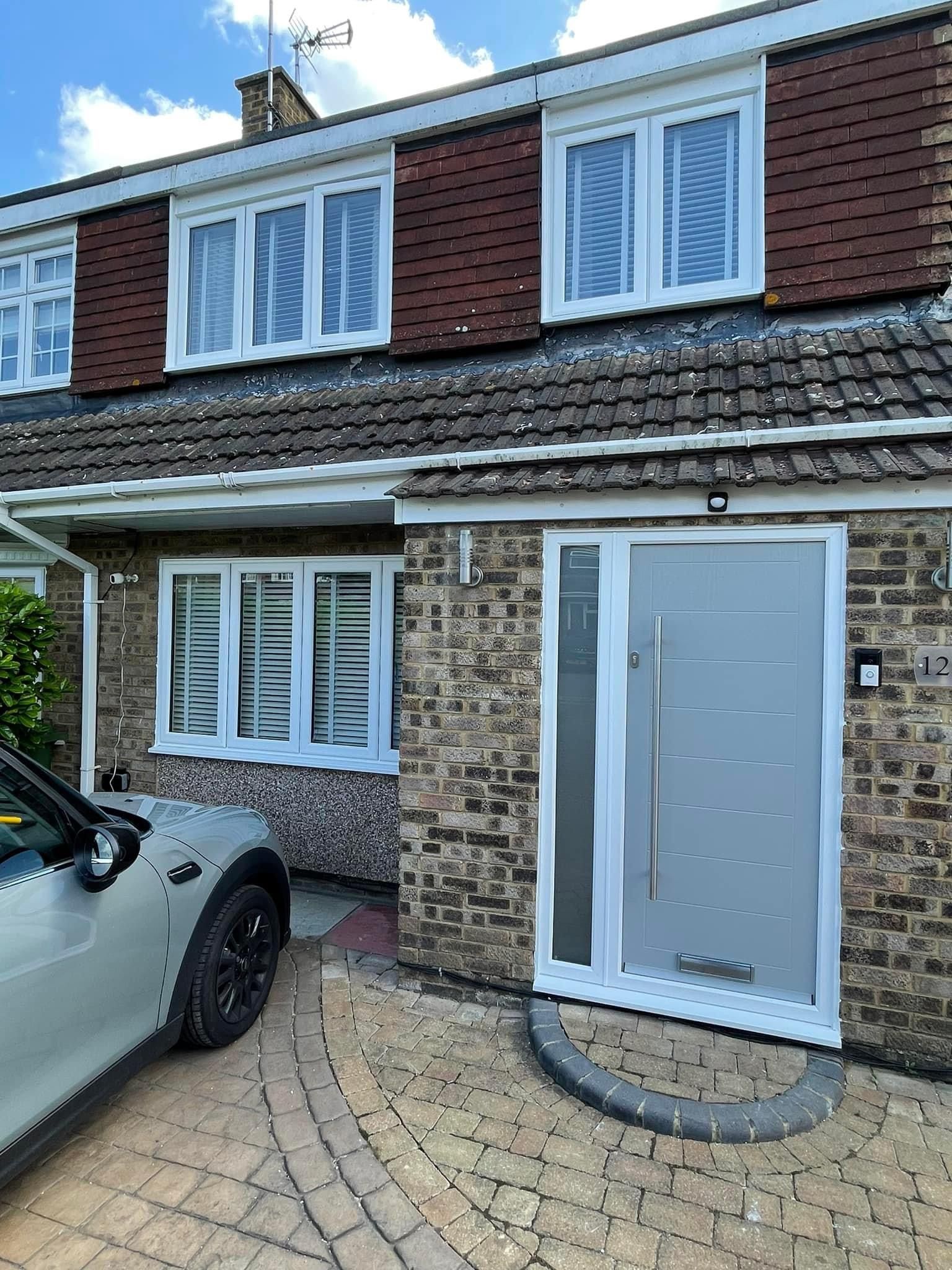 Gray front door with sidelight on a brick house; a car is parked in the driveway.