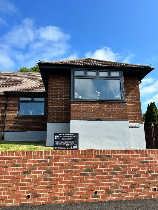 Brick house with gray accents and windows, a brown roof, and a low brick wall. Blue sky.