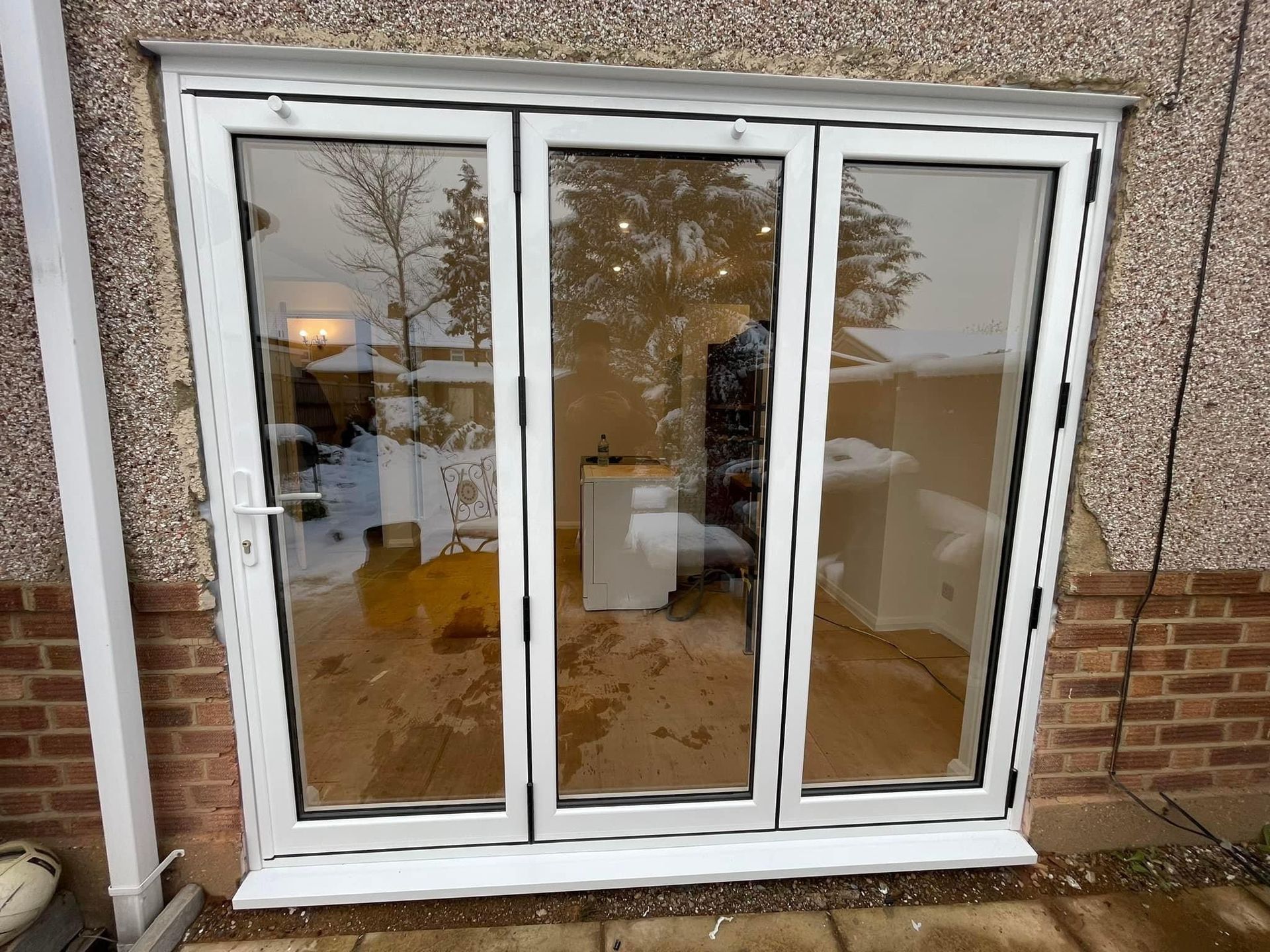 White framed folding glass doors, set into a brick and stucco exterior, reflect a snowy outdoor scene.