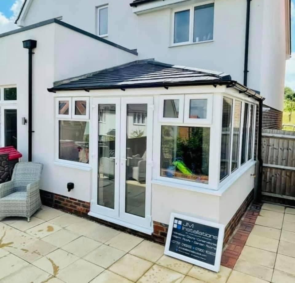 White conservatory extension on a house with glass windows and doors; patio with a chair.