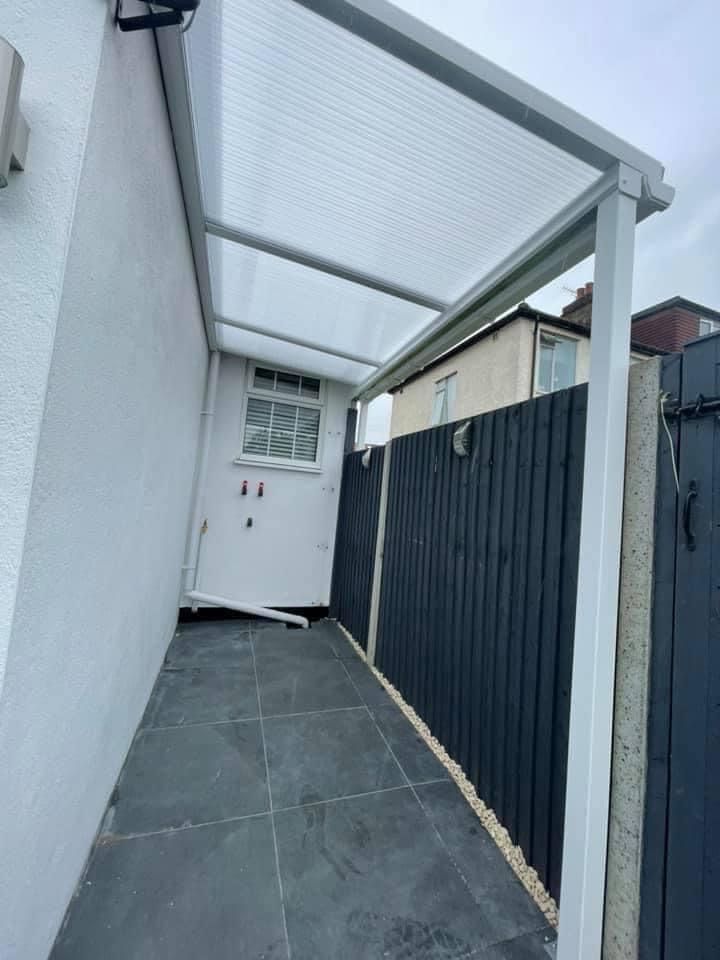 Covered outdoor walkway with gray tiled floor, white walls, and a black fence.