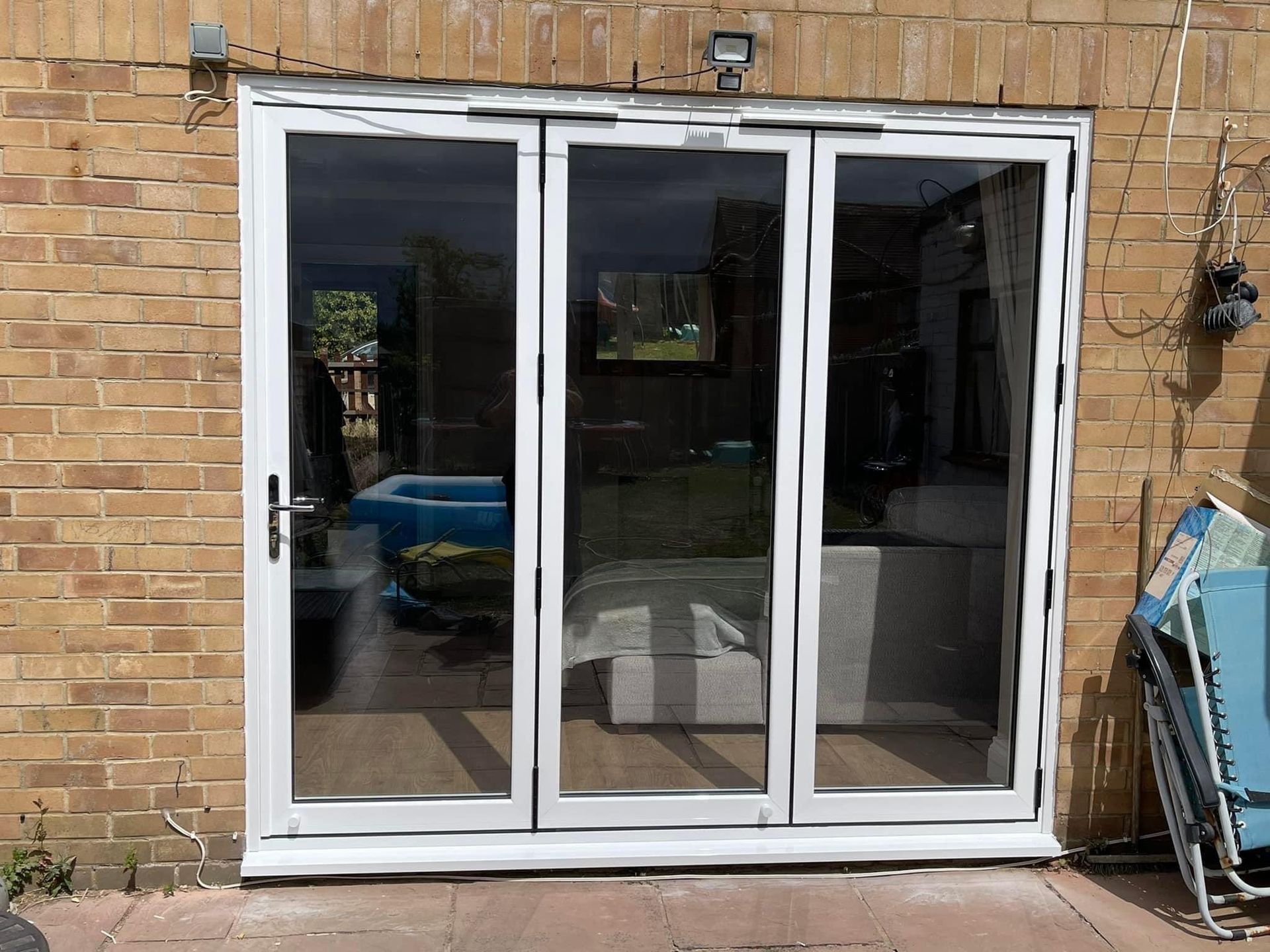 White framed glass folding doors on a brick wall, reflecting a living room and backyard with a pool.