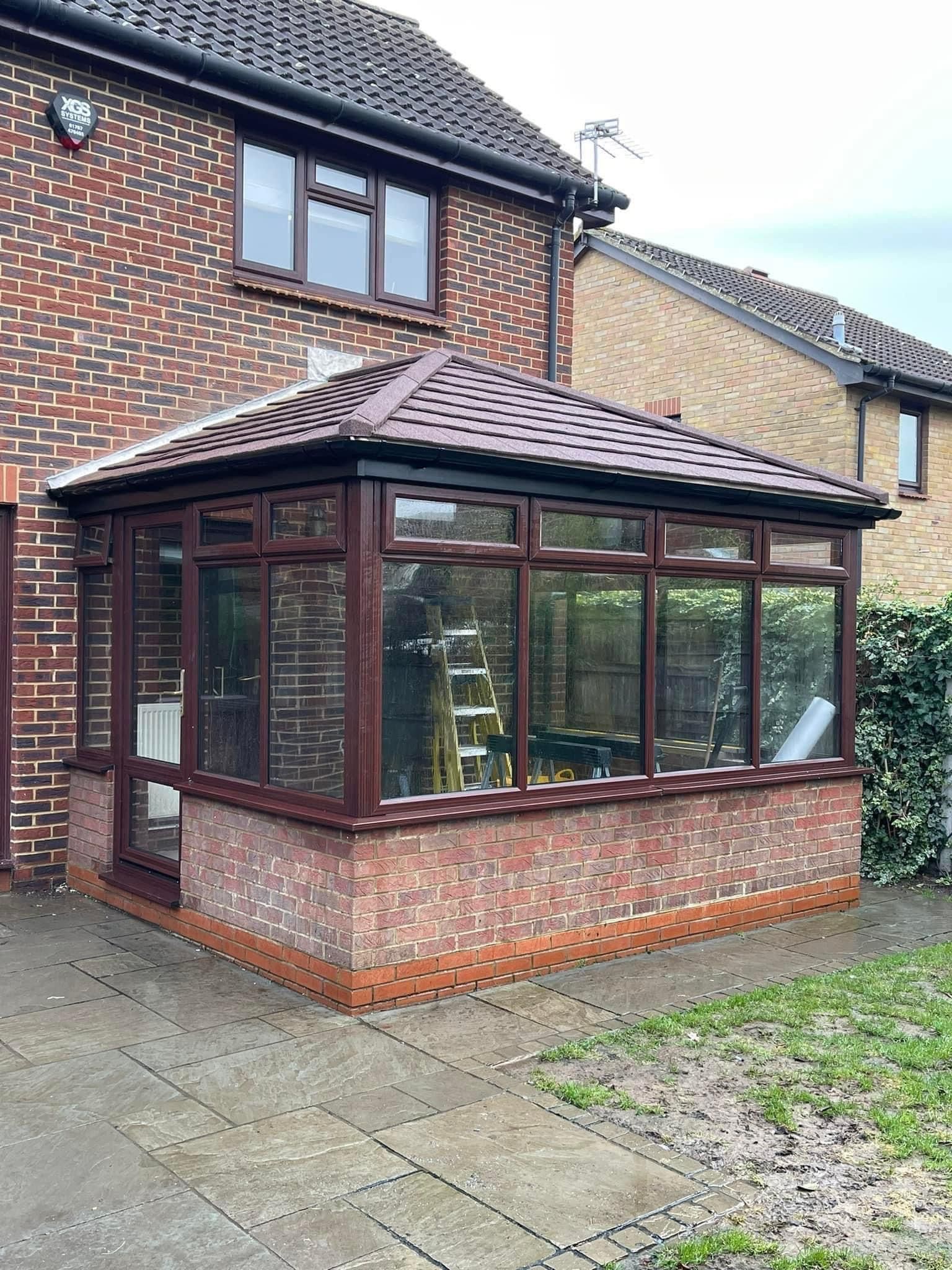 Brick house with a brown-framed conservatory. The conservatory has a brick base, glass windows, and a brown roof.