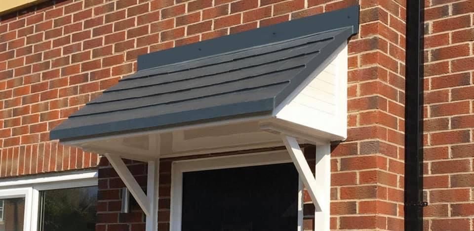 White-framed awning with a dark gray roof over a black door on a red brick house.