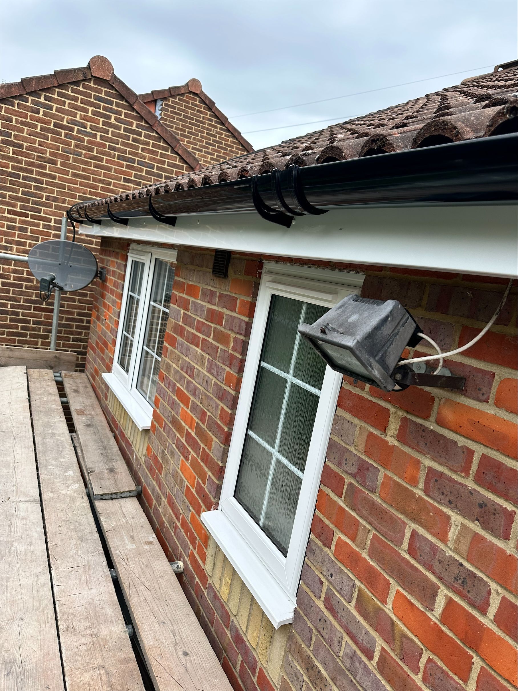 A brick house with a white window and a black gutter.