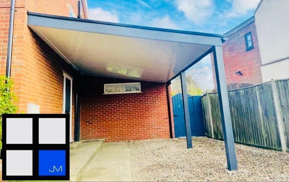 A carport attached to a brick building with a gravel driveway and blue gate.