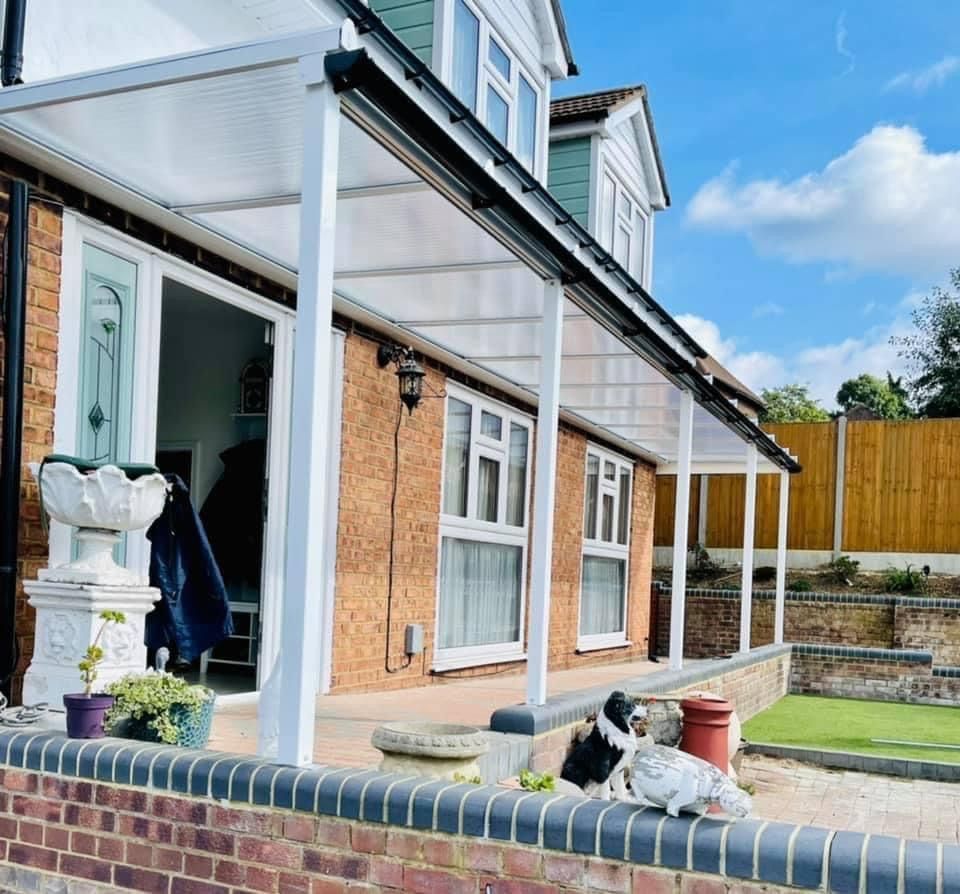 A house with a white awning, brick wall, and two dogs relaxing on the wall in front.