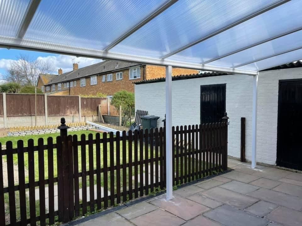 Covered patio with a brown picket fence and white support beams.