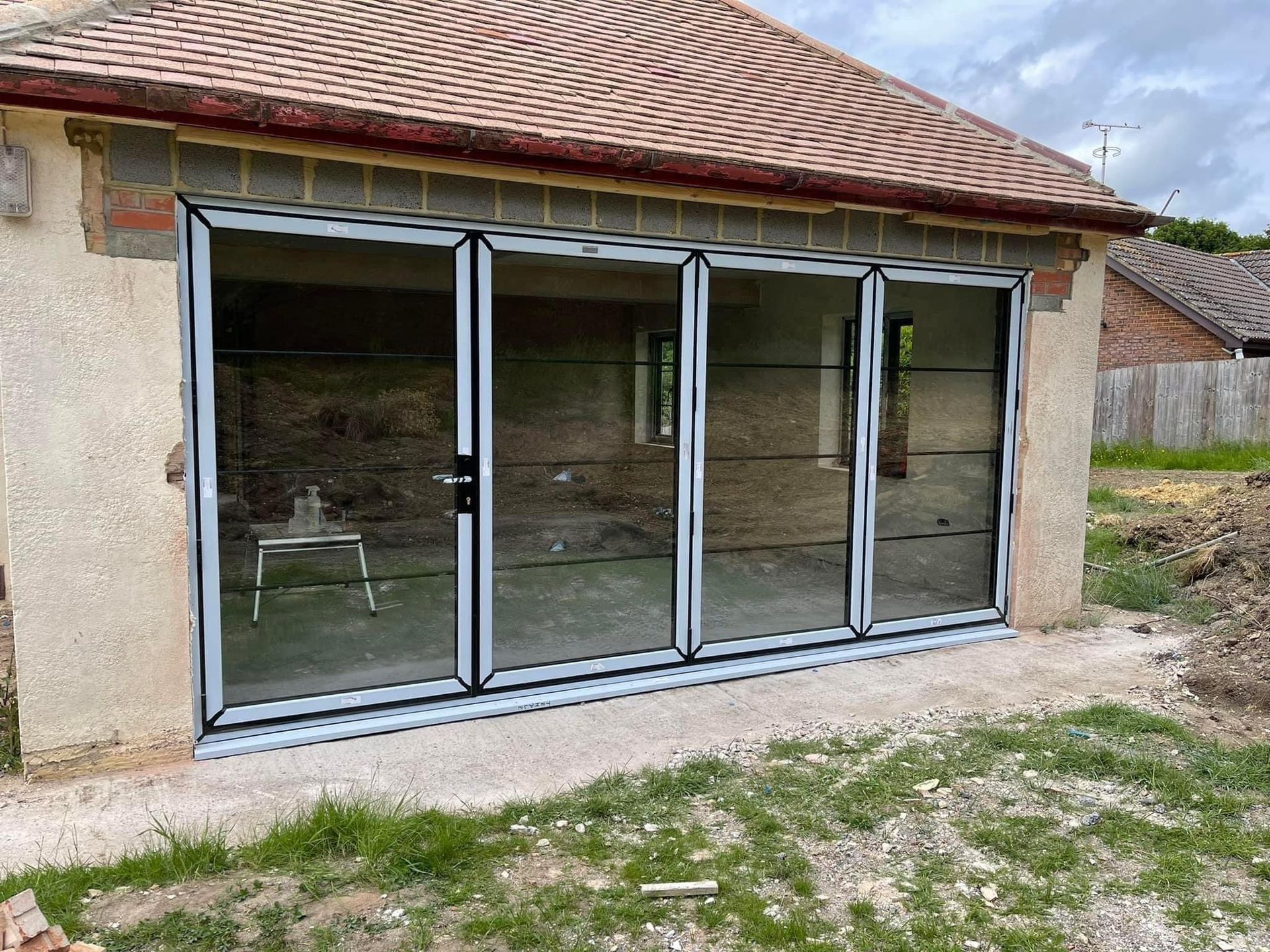 Exterior view of a building with four-panel folding glass doors. The building has a brick wall and a concrete base.