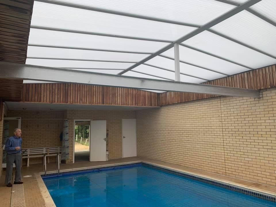 Indoor swimming pool with translucent roof, man standing near pool, brick walls, and wooden accents.