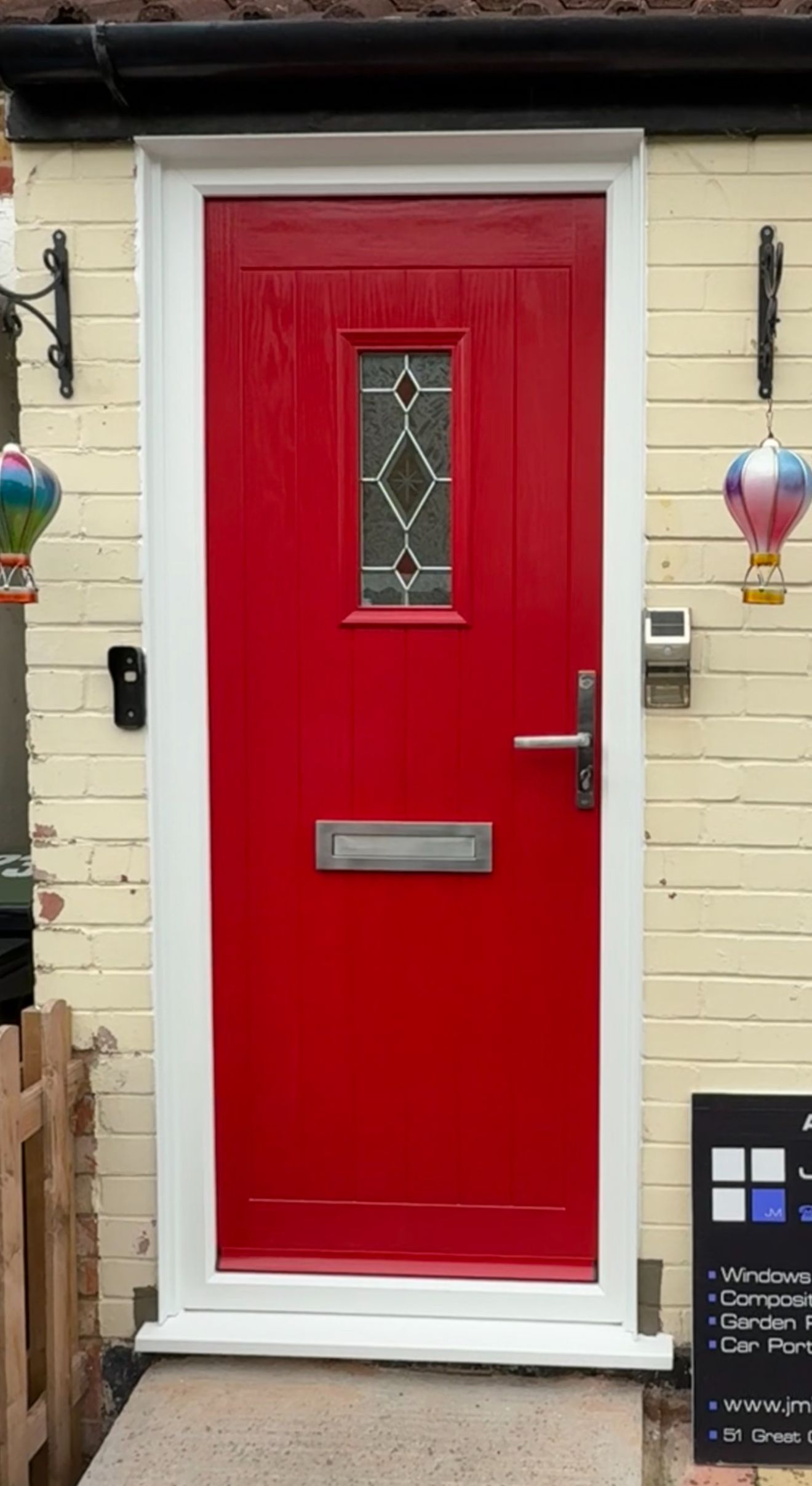 Red front door with glass panel, white trim, on a cream-colored brick facade.
