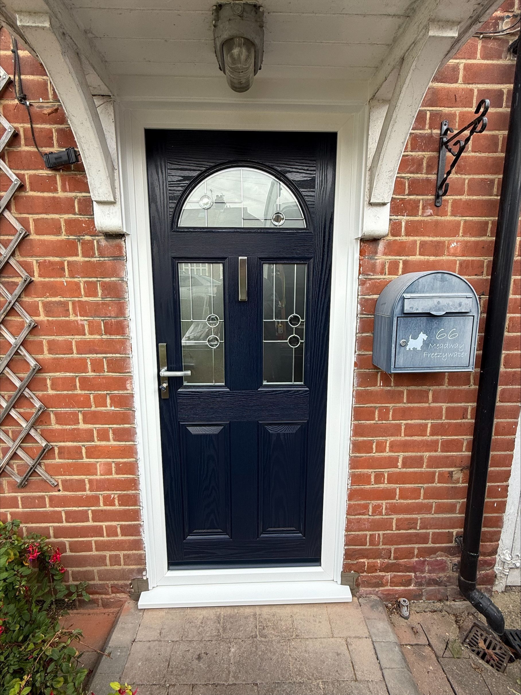 Dark blue front door with arched glass top, flanked by sidelights, set in brick with white trim.
