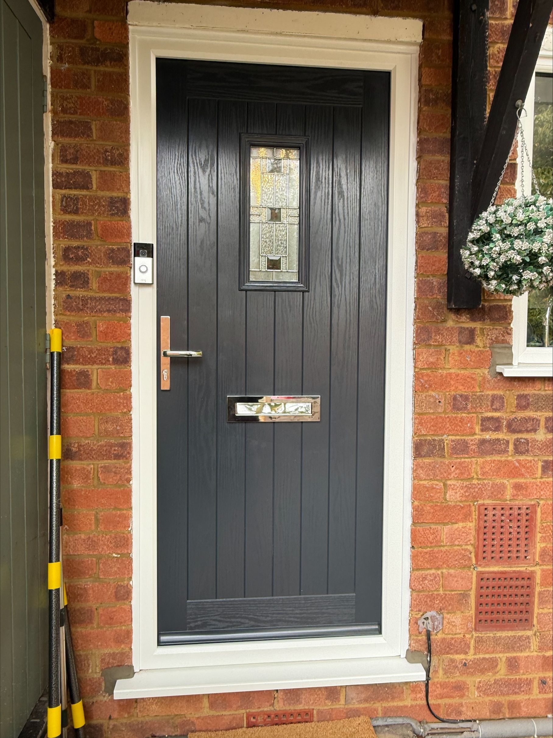 Gray front door with vertical grooves, rectangular glass panel, brass hardware, and a brick exterior.