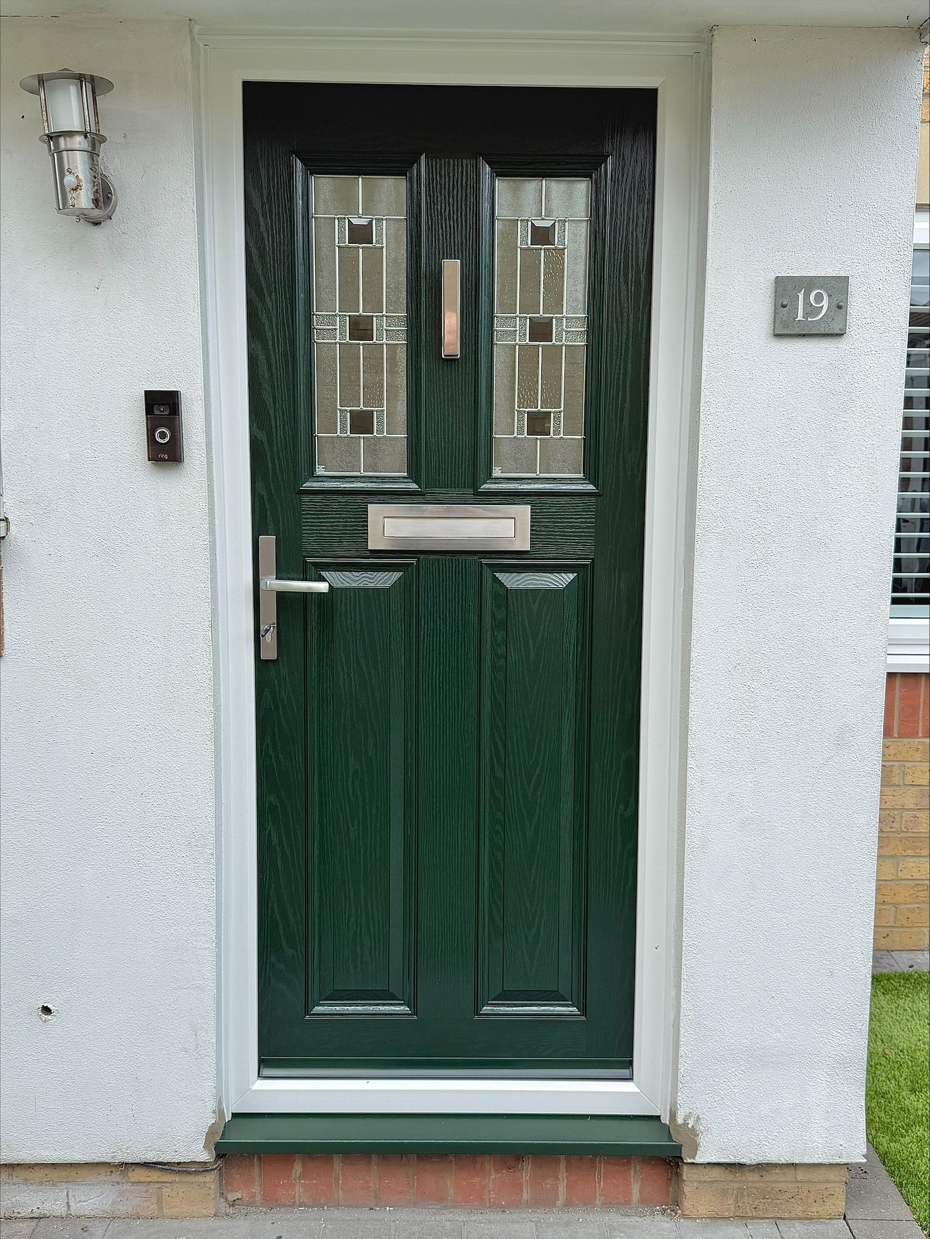 Green front door with glass panels, mailbox, and door handle set in white trim and stucco wall.