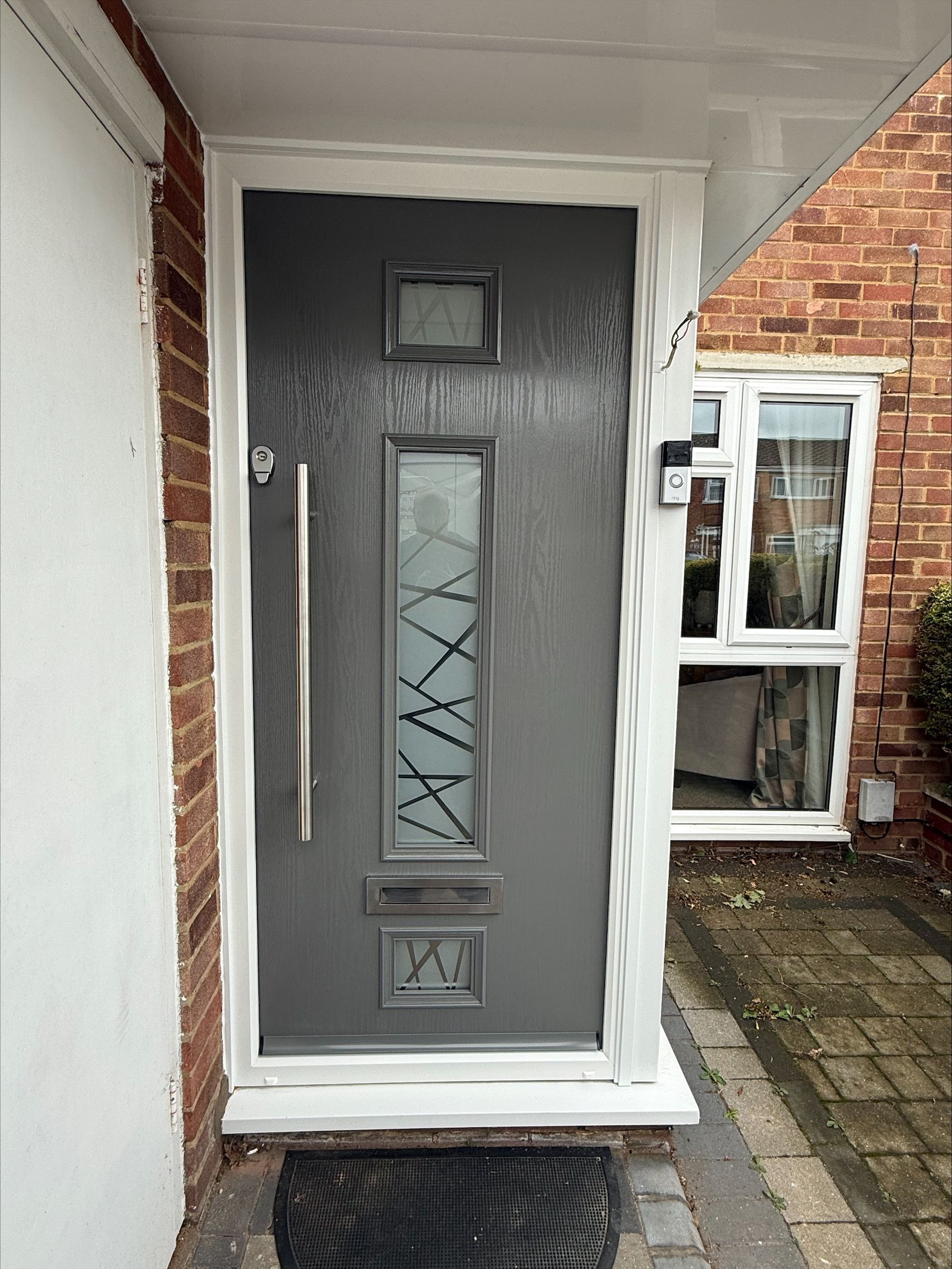 Gray front door with glass panel, silver handle, and brick exterior.