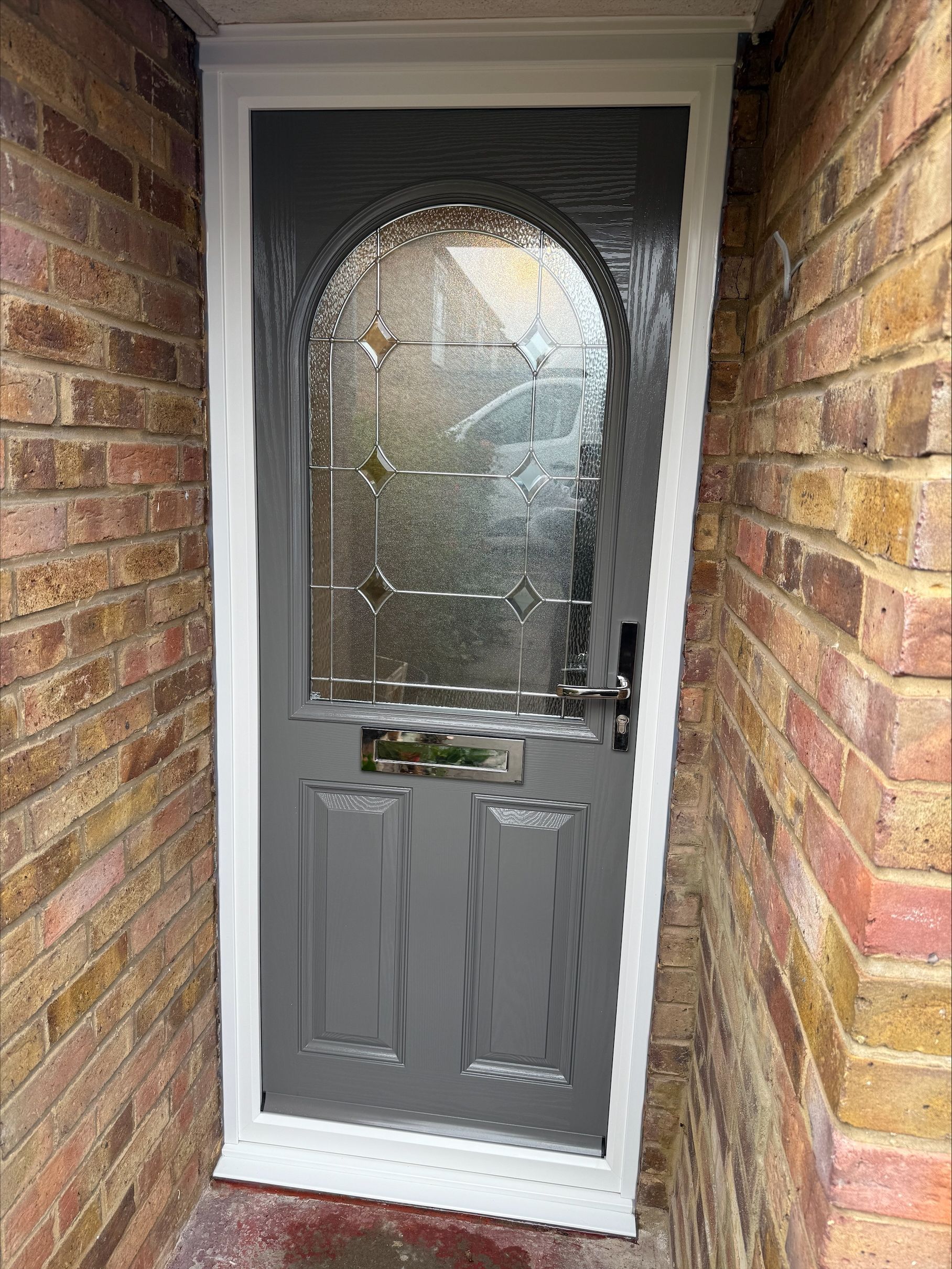 Gray front door with arched glass panel, set in a brick entryway.