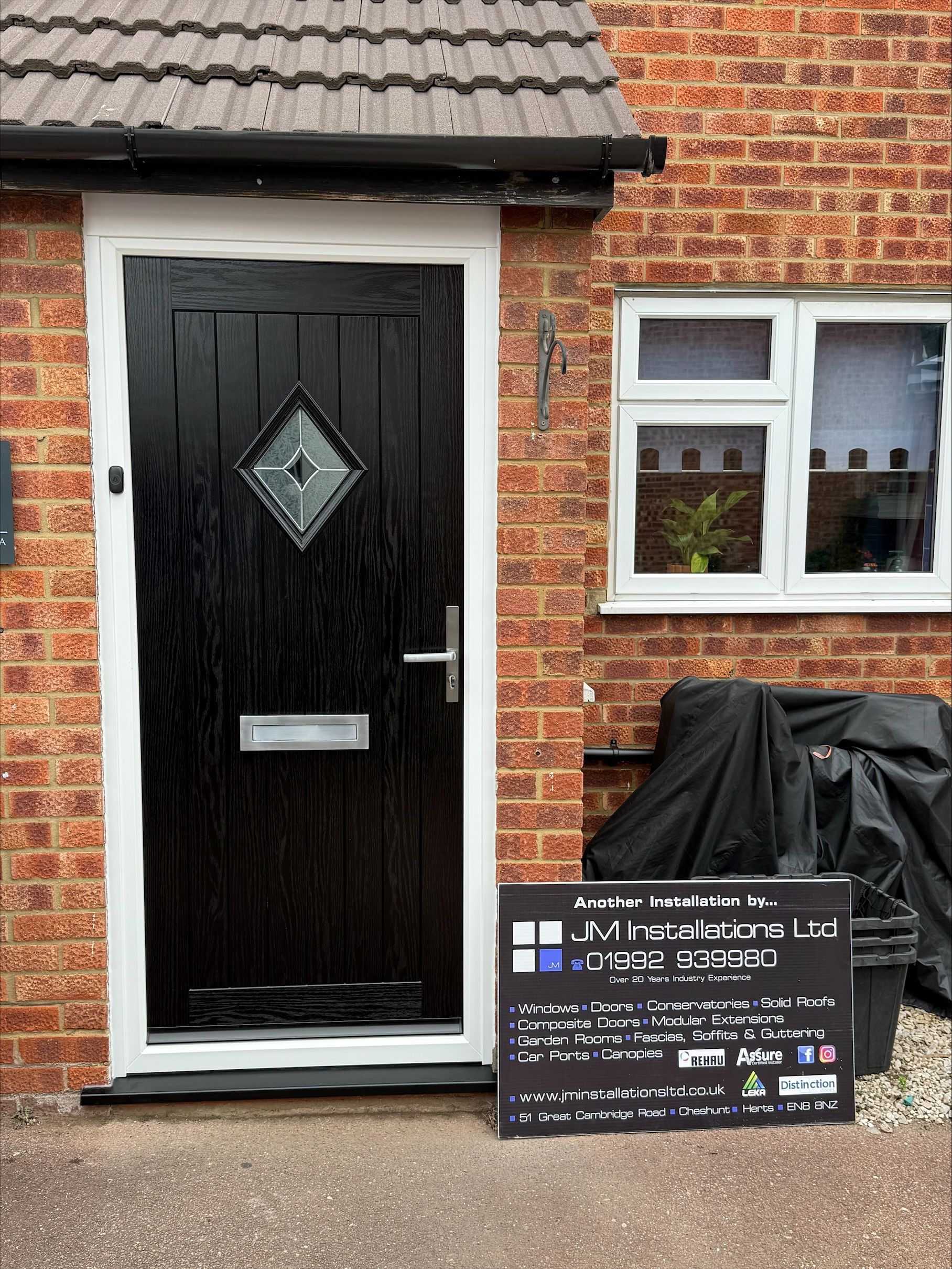 Black front door with diamond window, white trim, brick wall, small window, and sign.