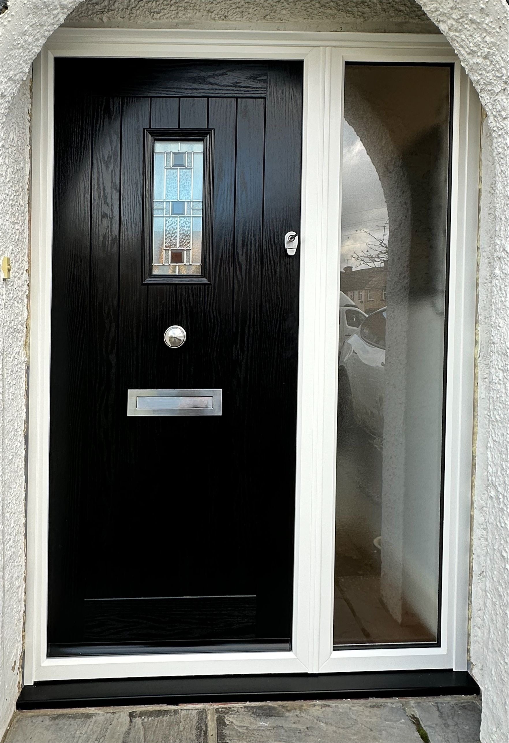 Black front door with small window, letter slot, and side window with white frame.