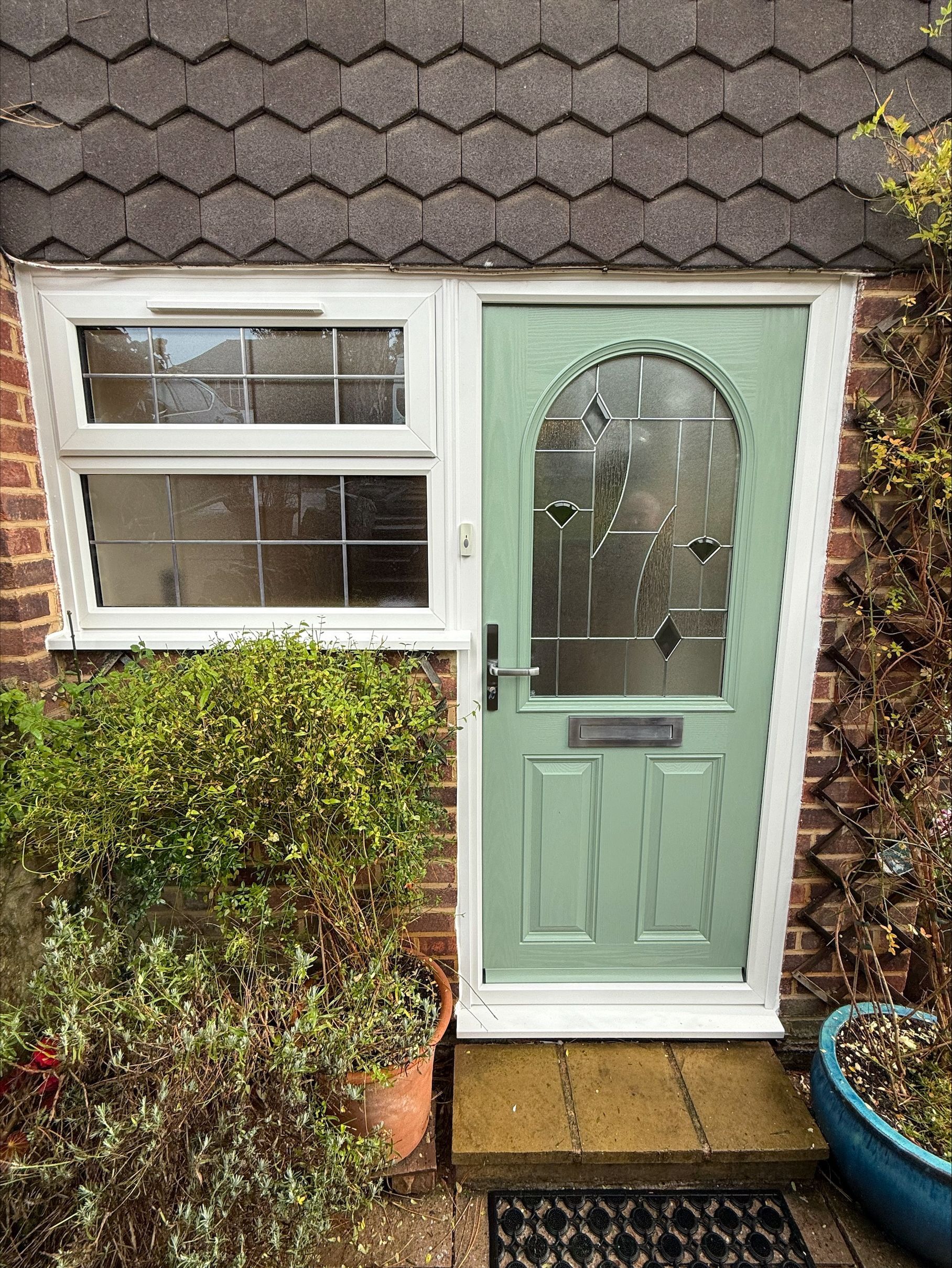 Green front door with decorative glass panel, small window, and brick facade.