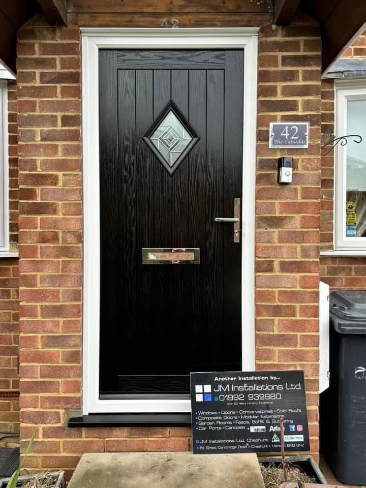 Black front door with diamond window, gold hardware, brick facade, address plaque, and sign.