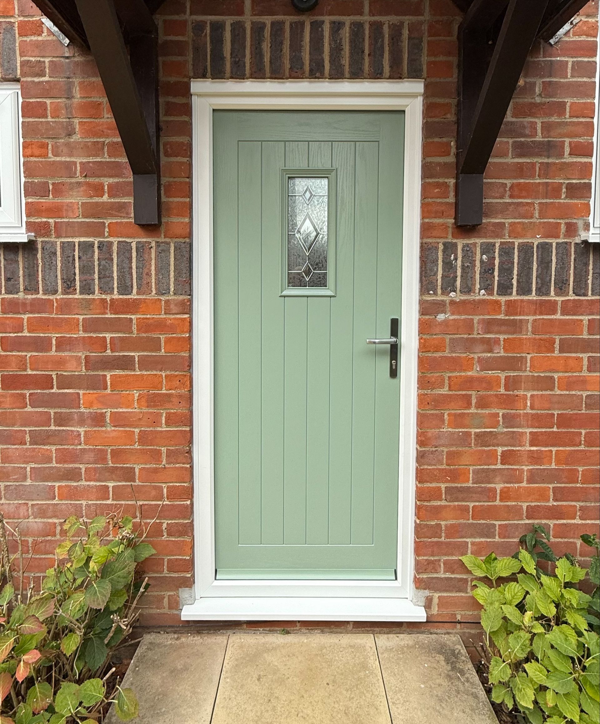 Green front door with glass panel, white frame, set in brick wall.